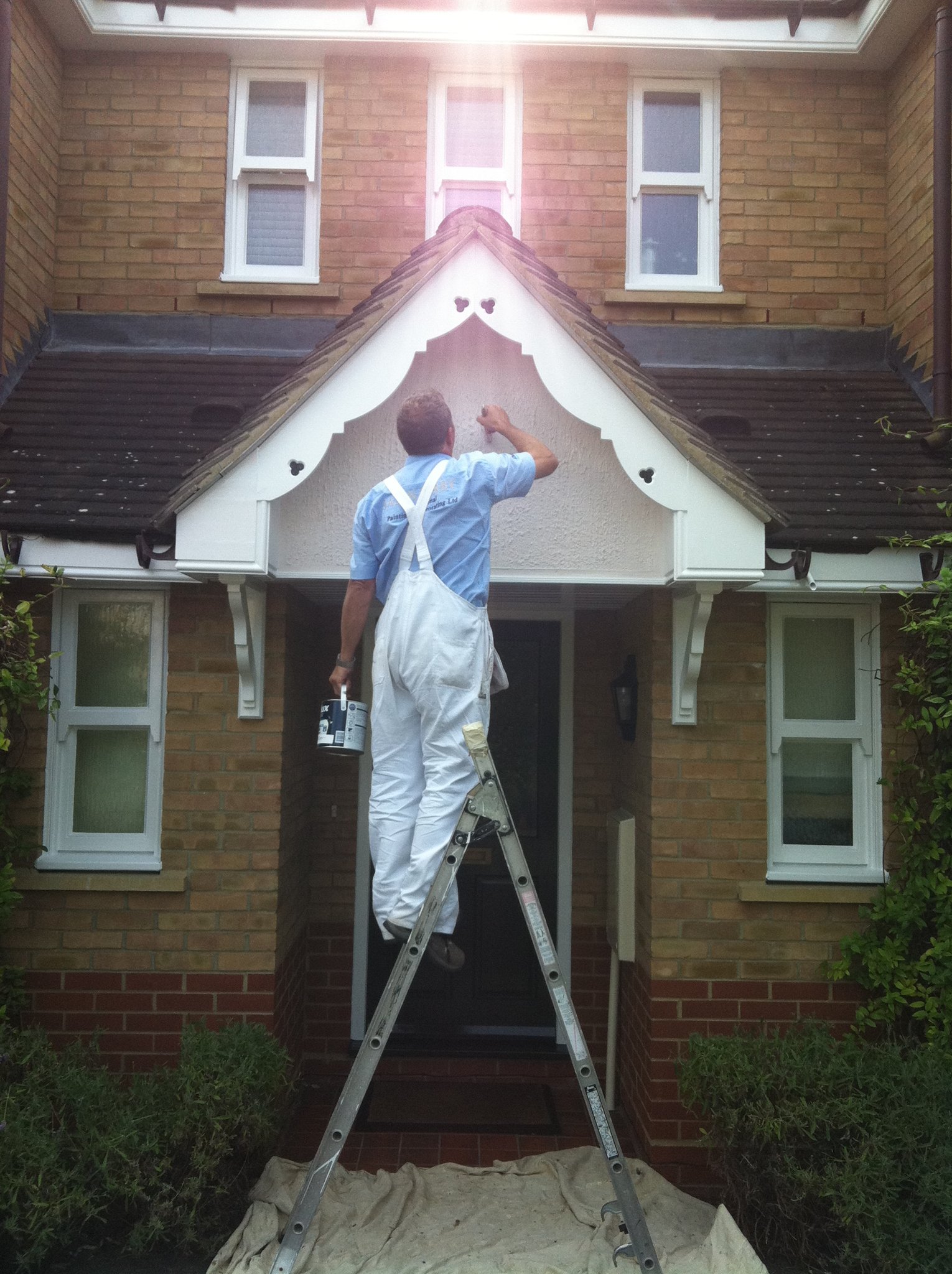 Decorator painting a porch gable in white overalls