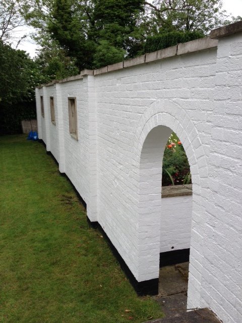 Long white painted garden wall with an arched opening