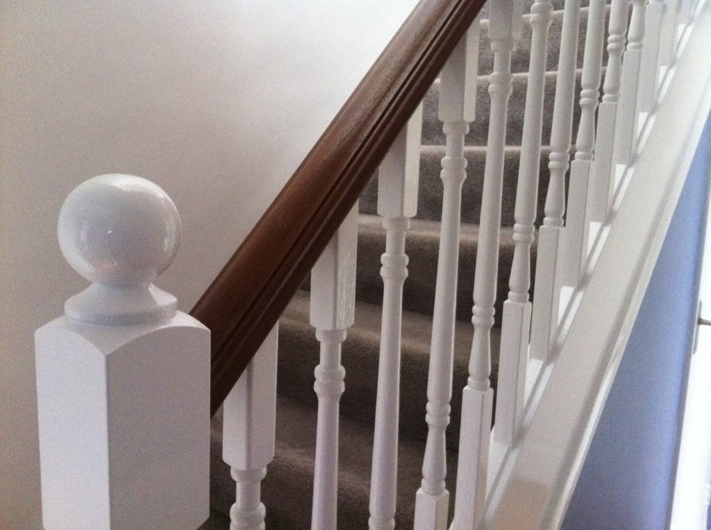 Turned newel post and white spindles under a dark handrail