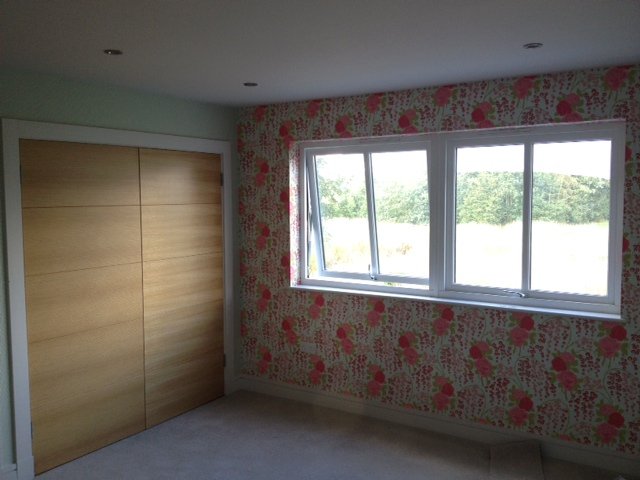 Bold floral wallpaper behind oak wardrobes