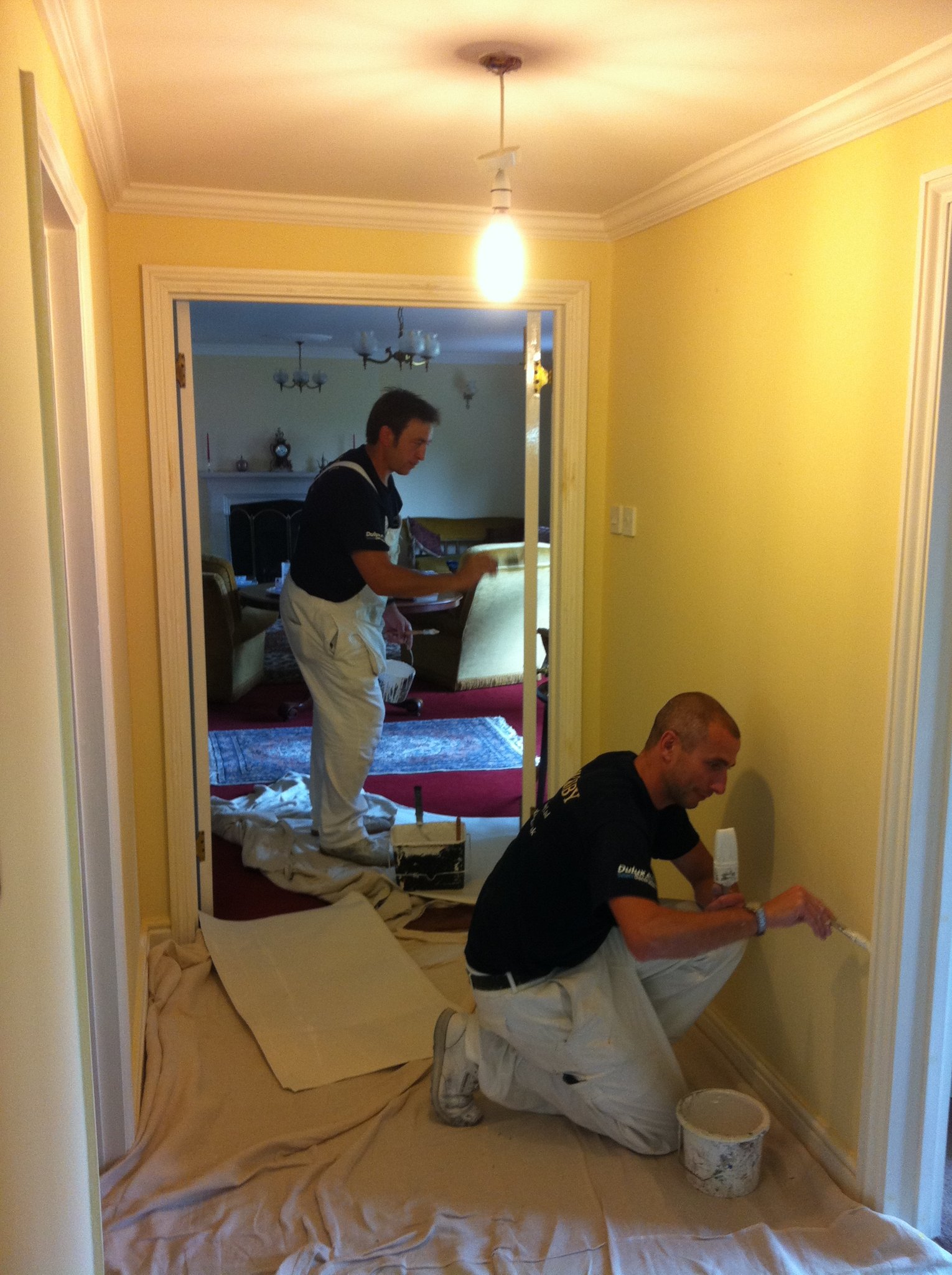 Two decorators painting a yellow hallway