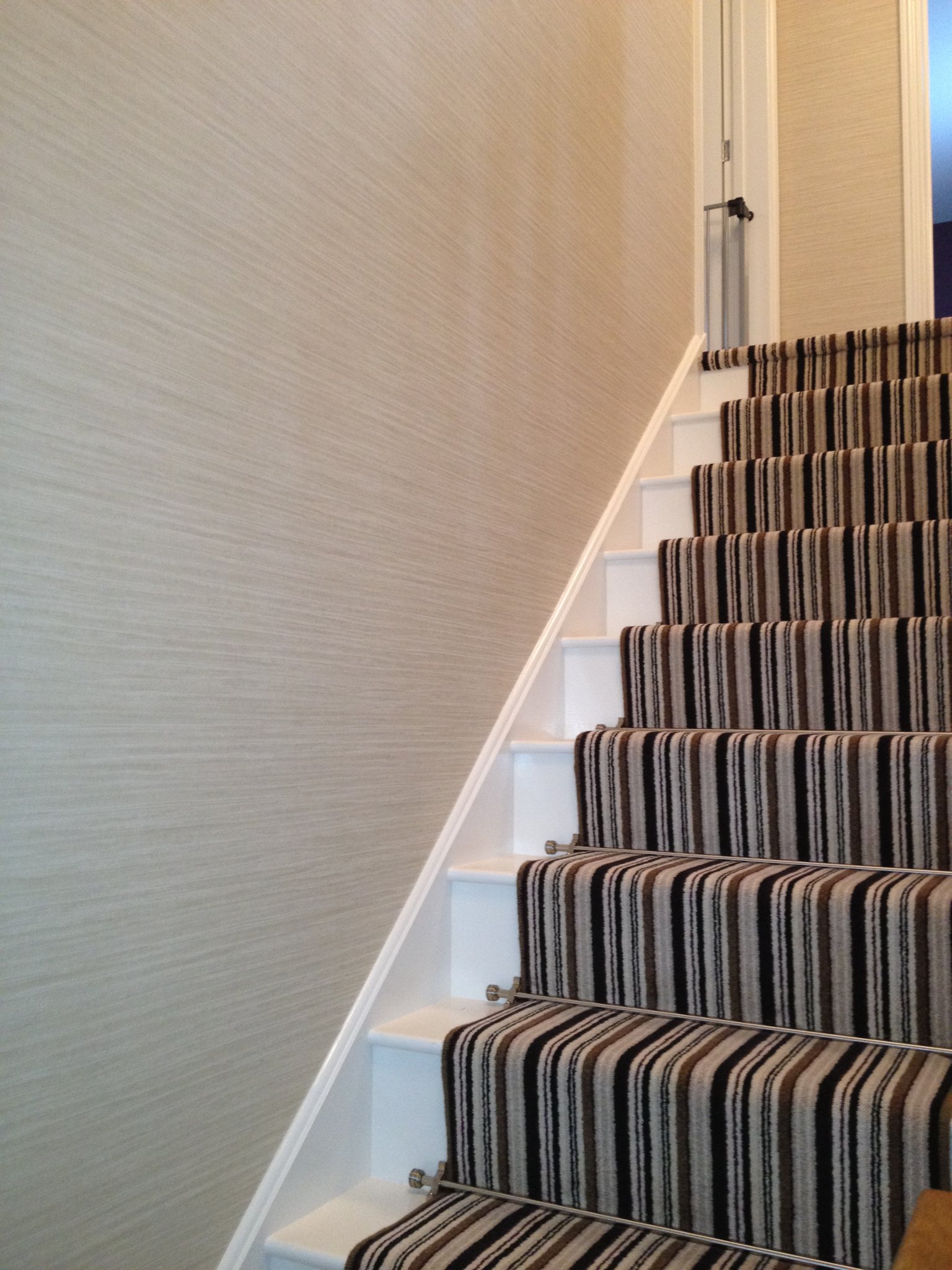 Staircase with a grasscloth papered wall and striped runner